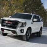 White 2021 GMC Yukon AT4 drives up a snowy road