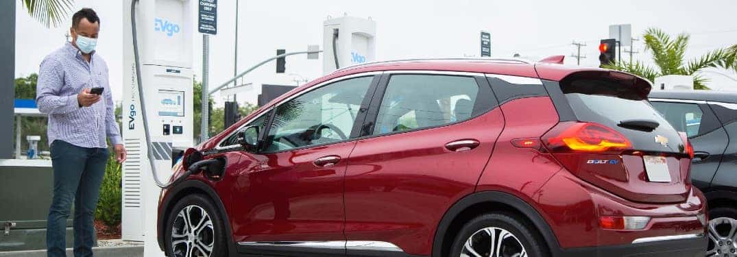 Man with facemask charges his red Chevy Bolt