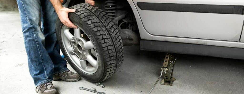 A person holding a car tire and wheel next to a car