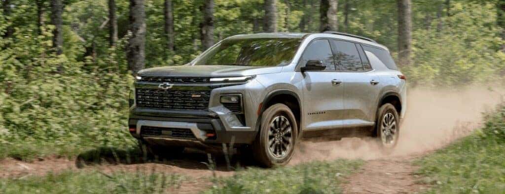 2024 Chevrolet Traverse driving on a dirt road by a forest
