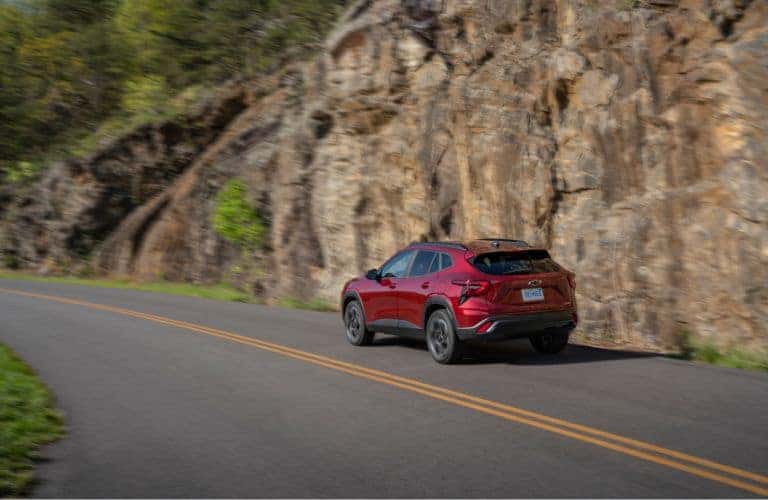 2024 Chevrolet Trax rear view driving on a road by a rock wall