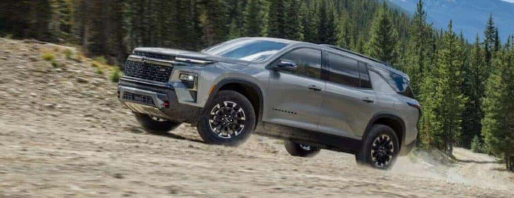 2024 Chevy Traverse driving on a sloped gravelly trail by a forest