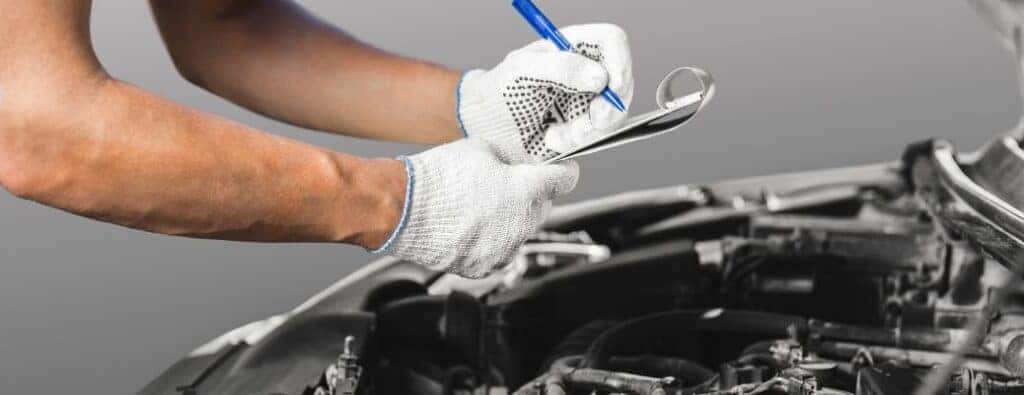 two white-gloved hands writing on a clipboard over a car engine