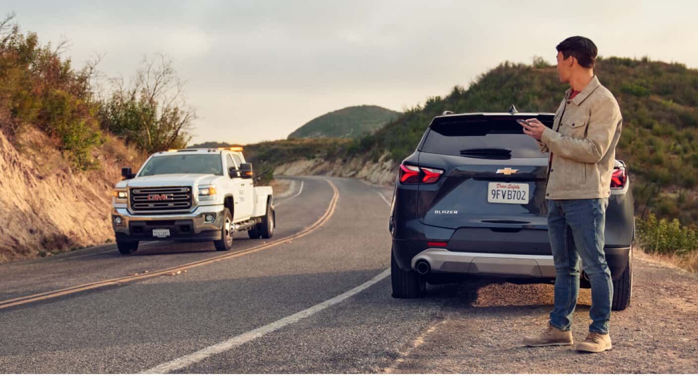Rear view of a Chevrolet Blazer awaiting an oncoming GMC Sierra tow truck in a canyon road setting.