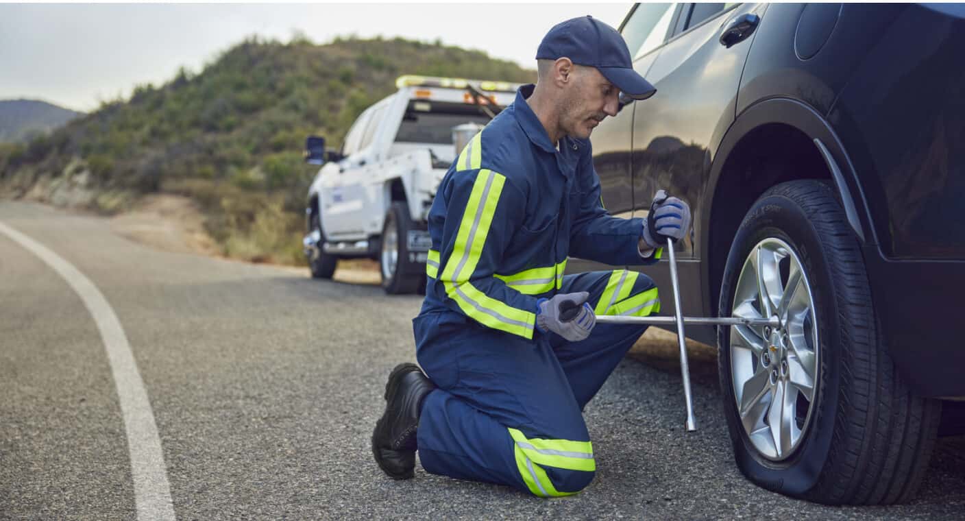 Close-up profile of a Chevrolet Blazer having a flat tire changed by roadside service on a mountain road.