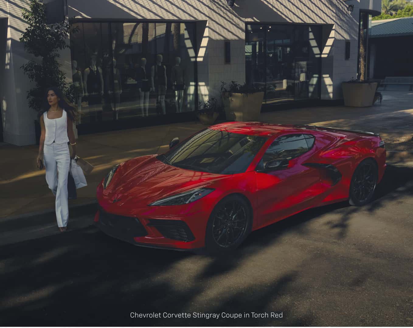 High-angle view of a Chevrolet Corvette Stingray Coupe in Torch Red parked street side near storefront shadows.