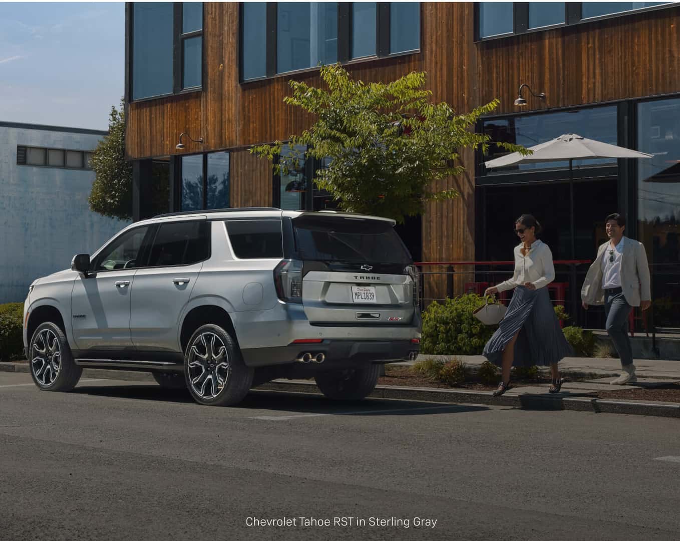 Three-quarter rear view of a Chevrolet Tahoe RST in Sterling Gray Metallic parked outside a modern urban building.
