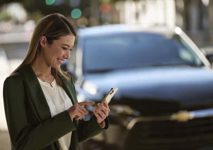 Front view of a Chevrolet Equinox with a woman using a smartphone in an outdoor urban setting.