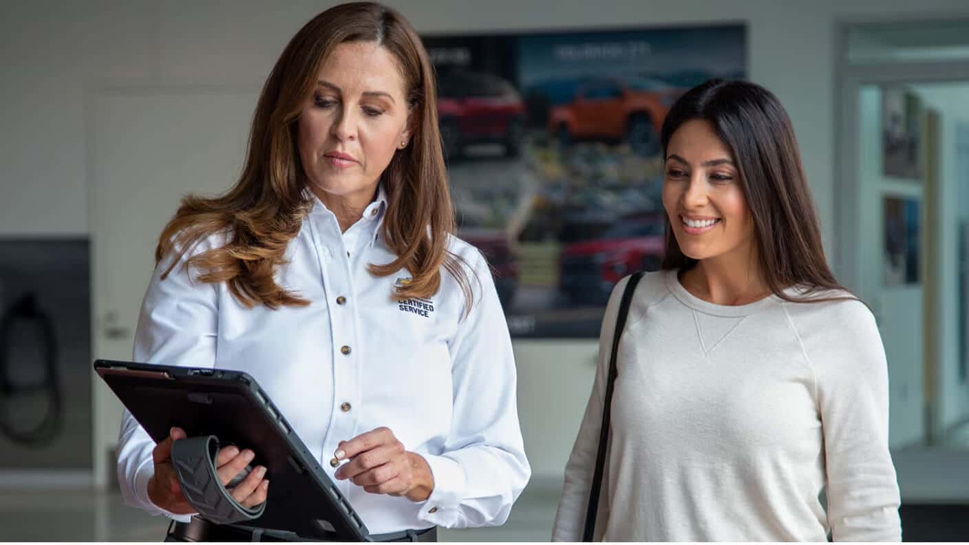 Chevrolet Certified advisor showing a tablet to a smiling customer inside a dealership showroom.