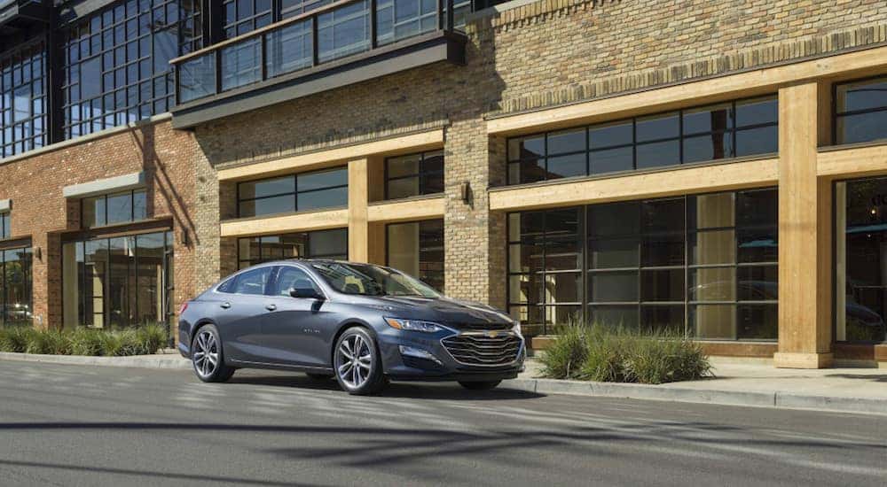 A grey 2019 Chevy Malibu in front of a large brick and wood building