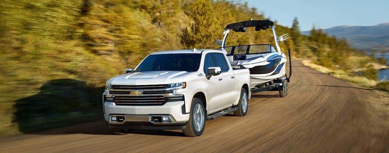 White 2019 Chevy Silverado towing boat on winding mountain road, lake to side