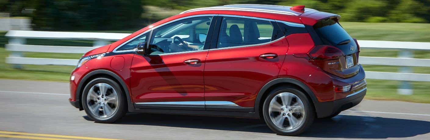 Red 2020 Chevrolet Bolt EV driving by white fence