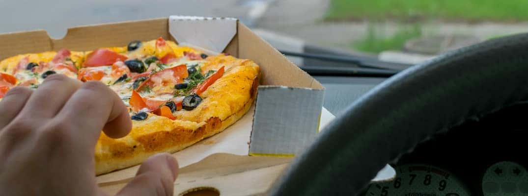 Driver grabbing a pizza from the dashboard of a car