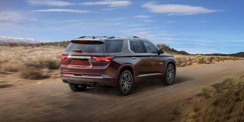 A maroon 2022 Chevy traverse driving on a dirt road through desert terrain
