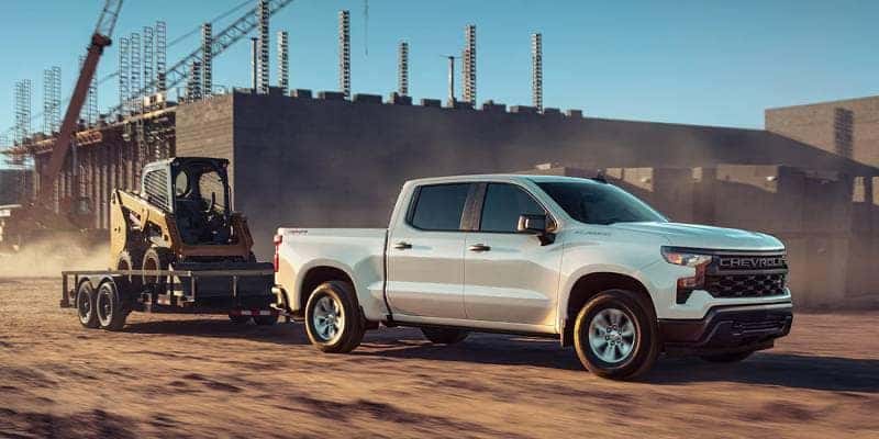 2023 Chevy Silverado Towing features include a max payload of 16,000 pounds. This is demonstrated in this photo by a Silverado pulling a large excavator on a trailer.