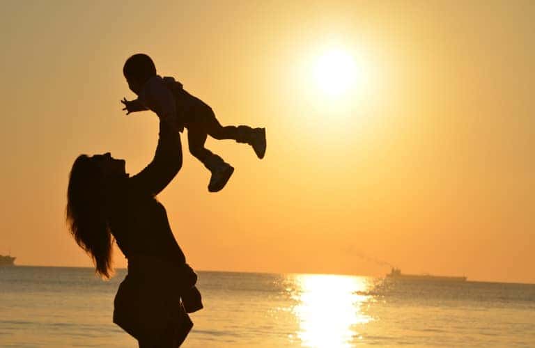 A mom holding her baby up with a sunset behind them.