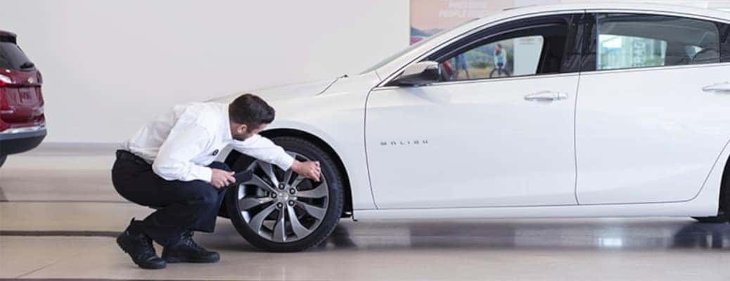 A man checking the tires on a new Chevy Malibu, which is one of the recommended things to do for summer car care 2023.