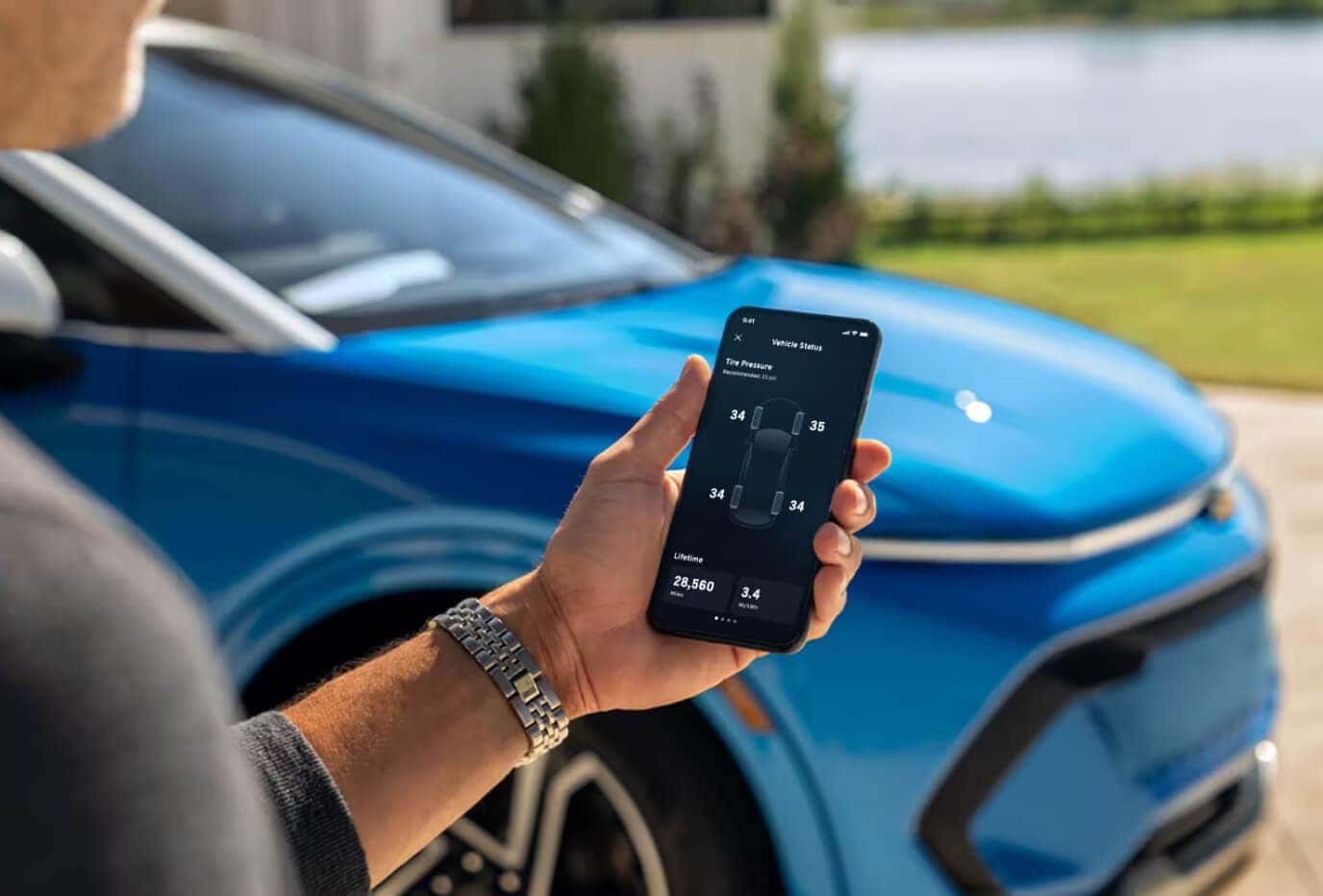 Close-up of a smartphone showing the myChevrolet app tire pressure screen next to a blue Equinox.