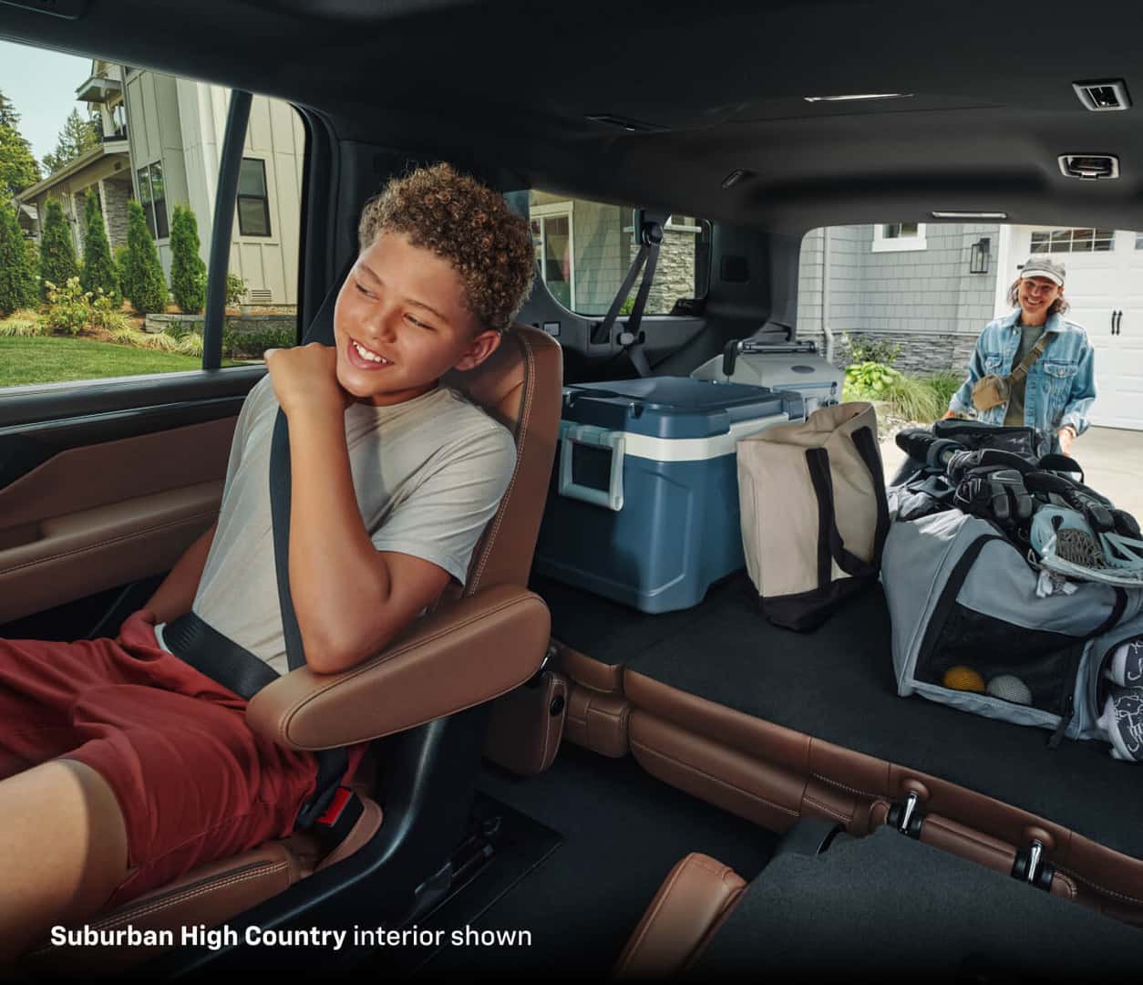 2025 Chevrolet Suburban High Country interior with a child seated beside folded cargo space loaded with outdoor gear.