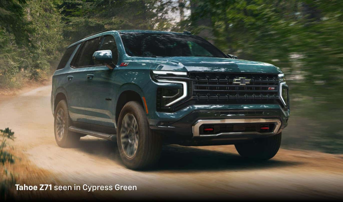 2025 Chevrolet Tahoe Z71 in Cypress Green, front three-quarter view driving on a dusty forest road.