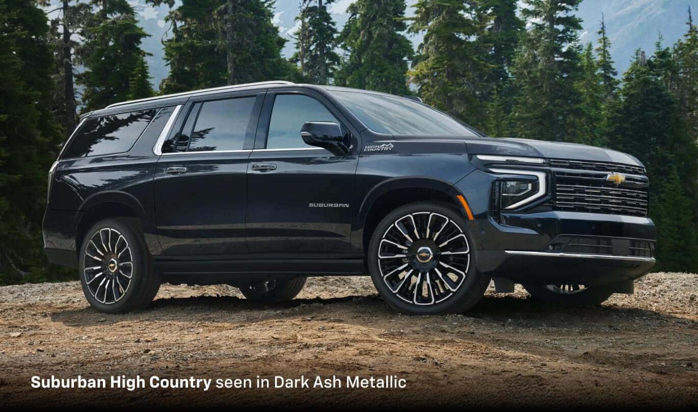 2025 Chevrolet Suburban High Country in Dark Ash Metallic, front three-quarter view on a scenic evergreen hilltop.