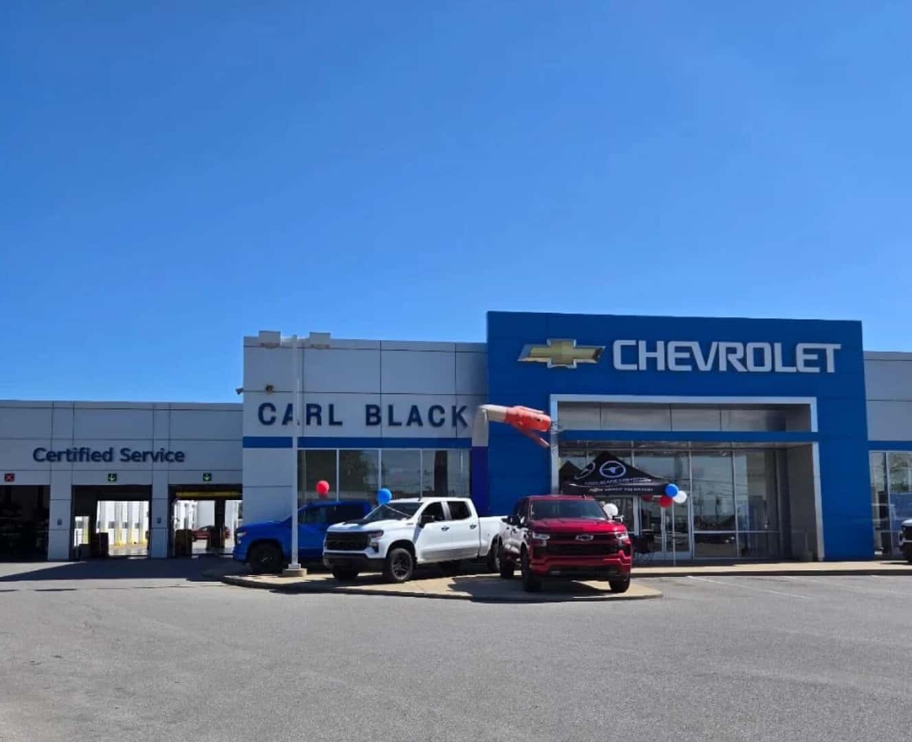 Front view of white and red Chevrolet Silverado trucks outside a Carl Black dealership.