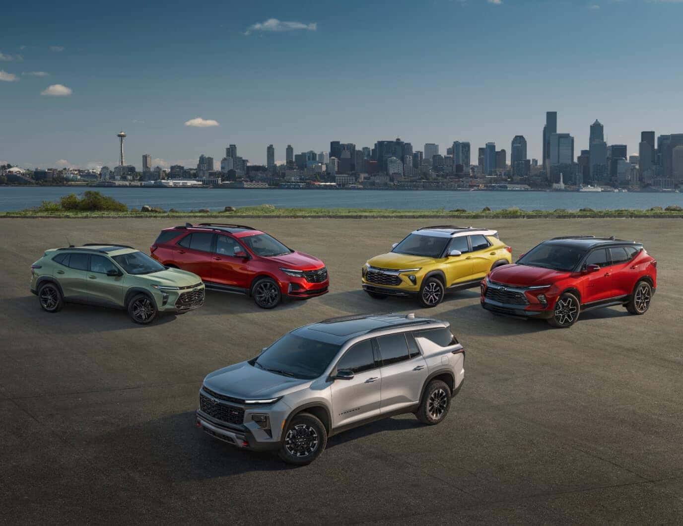 Front three-quarter view of Chevrolet SUV lineup in various colors with a city skyline background.