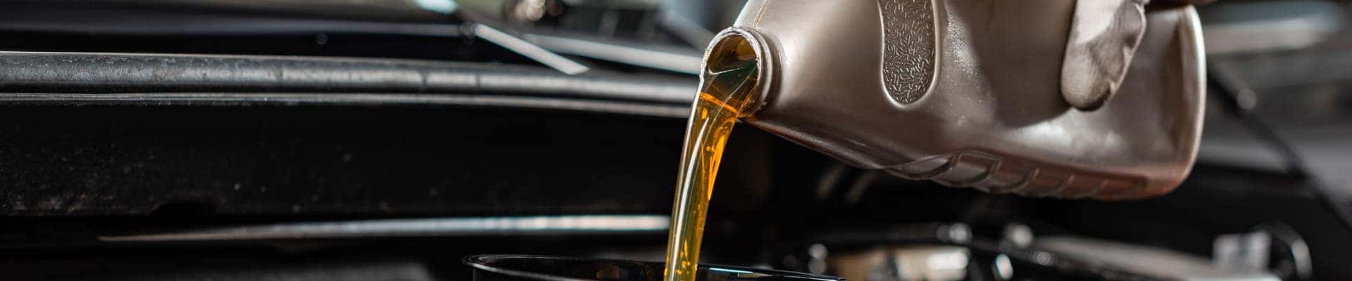 Motor oil being poured from a container into a vehicle engine during an oil change.