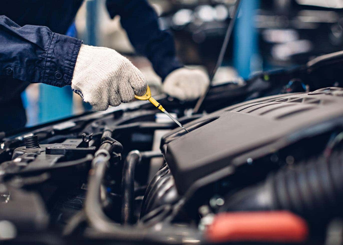 Technician checking a vehicle’s engine oil level with a dipstick.