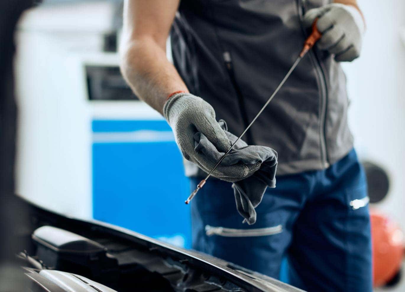 Technician wiping a vehicle’s engine oil dipstick with a cloth during an oil level check.