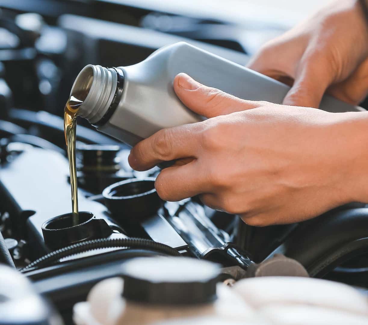 Motor oil being poured from a bottle into a vehicle’s engine during an oil change.