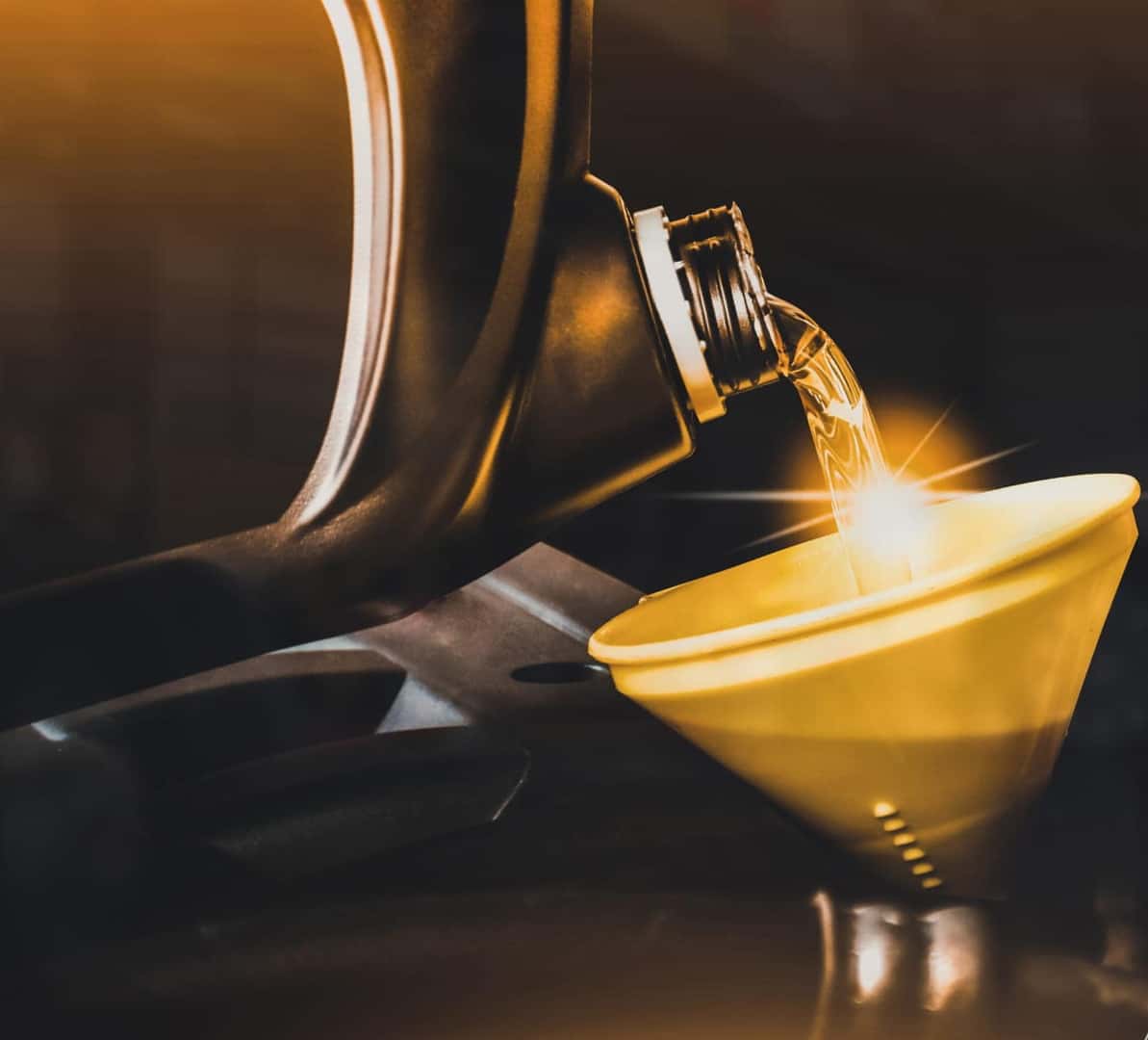 Motor oil being poured from a container into a yellow funnel during an oil change.