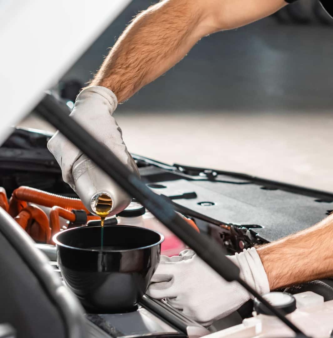 Technician pouring motor oil through a funnel into a vehicle’s engine during an oil change.