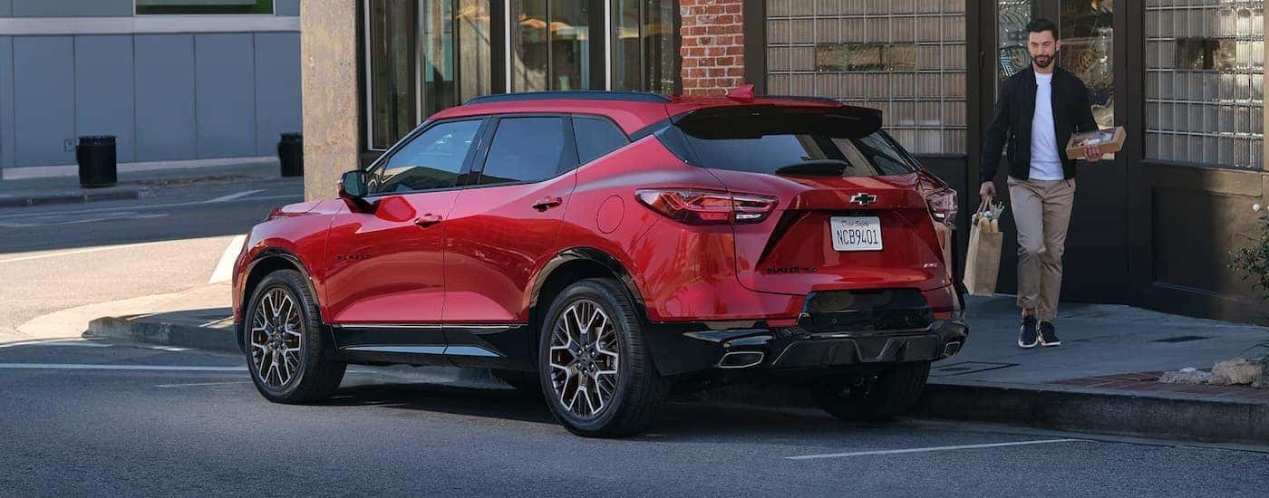 Rear view of a red 2025 Chevy Blazer EV parked by a city curb.