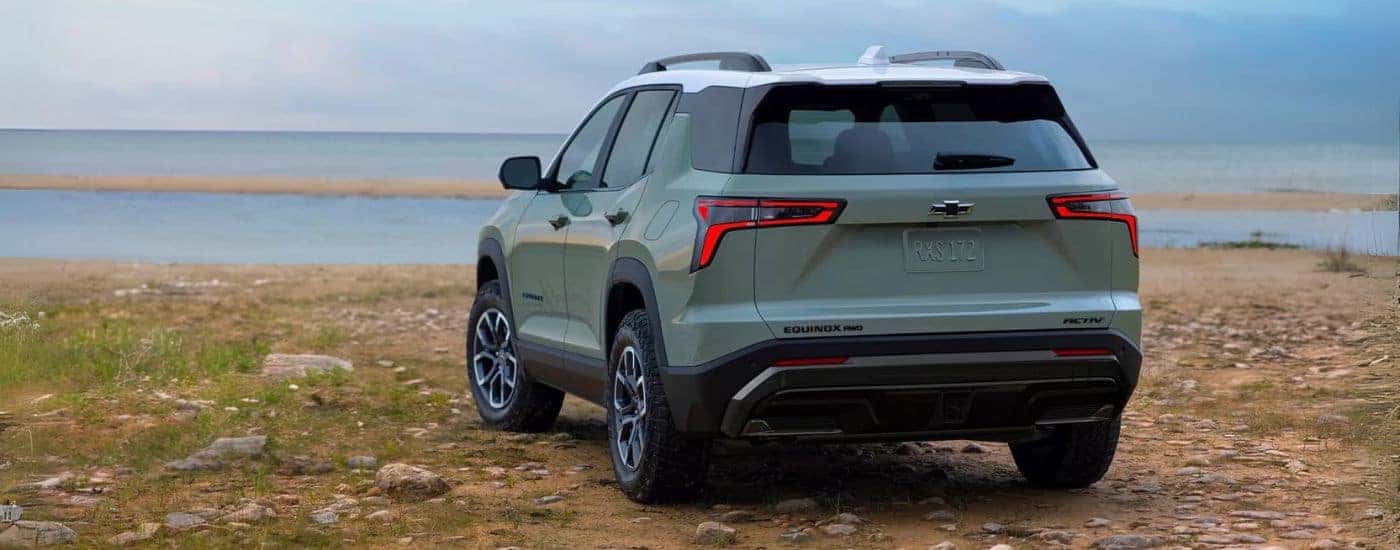 Rear view of a green 2025 Chevy Equinox ACTIV parked off-road after visiting a dealer with a Chevy Equinox for sale.