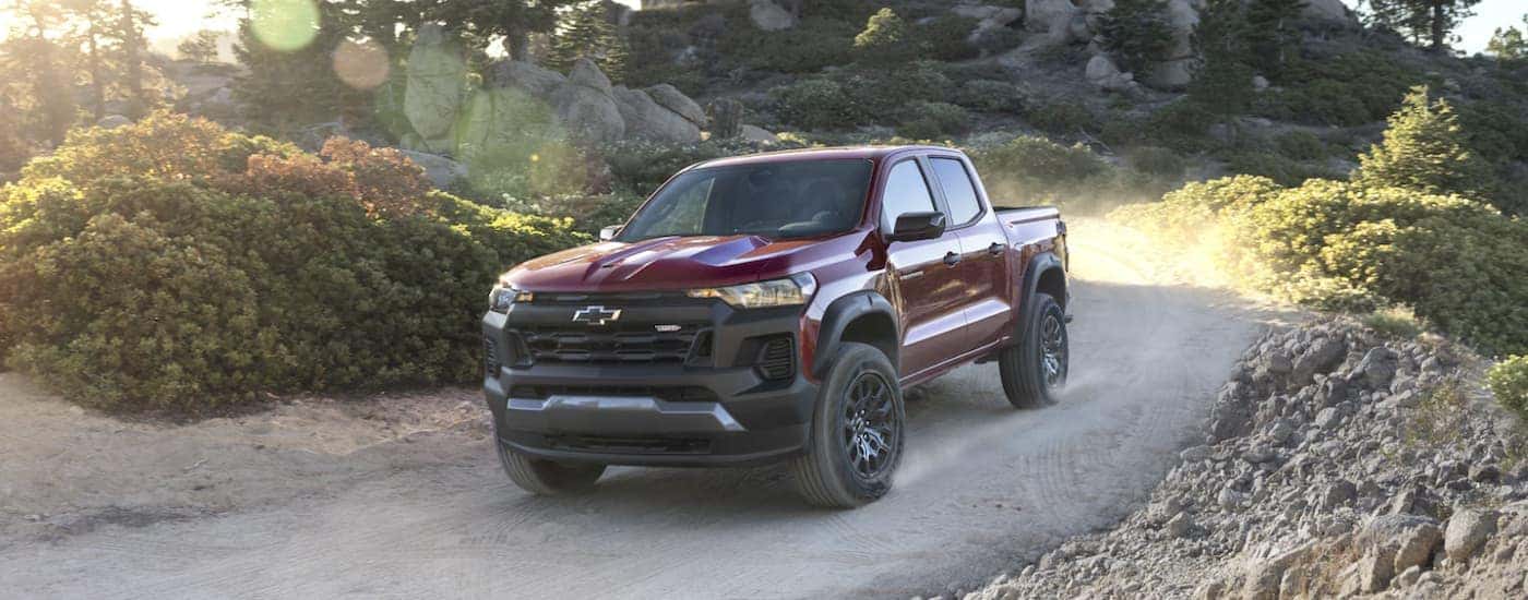 A red 2023 Chevy Colorado Trail Boss is shown driving off-road after viewing a used Chevy for sale.