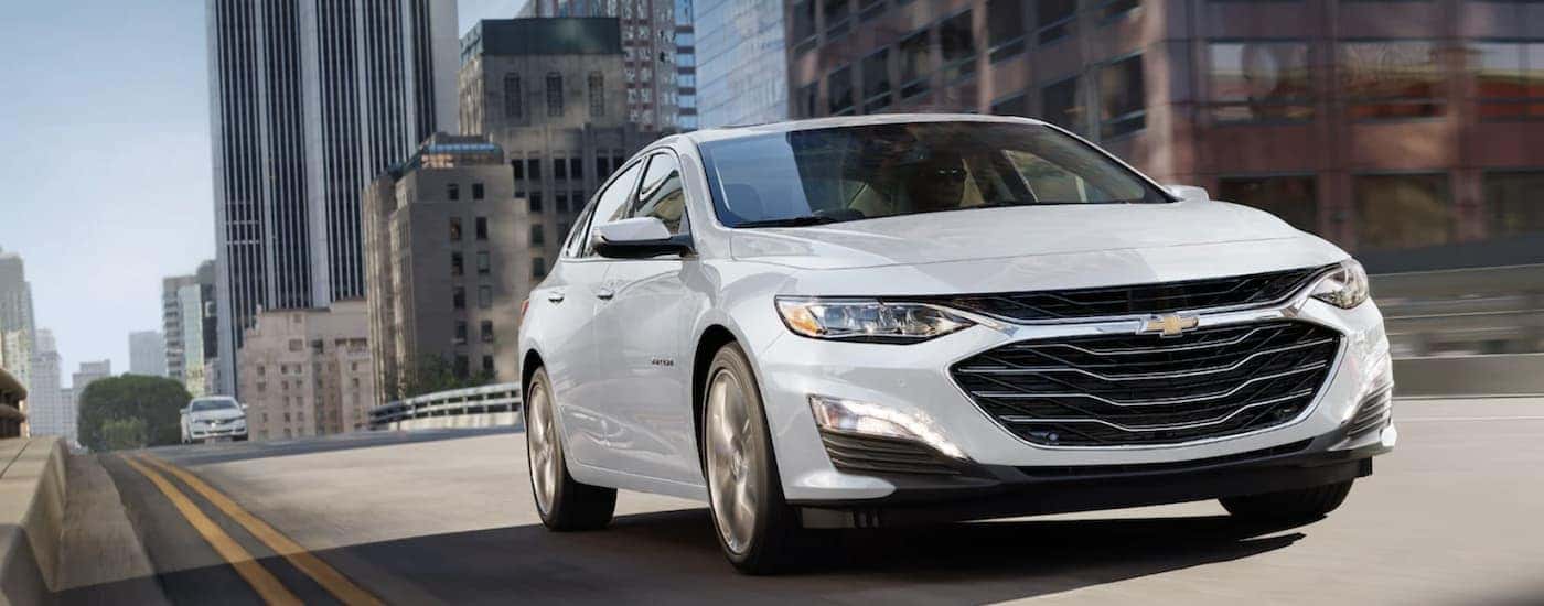A white used 2022 Chevy Malibu driving in a city
