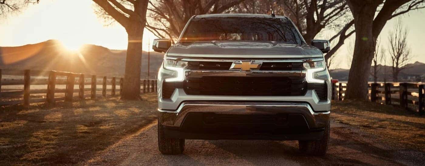 Front of a silver 2025 Chevy Silverado 1500 for sale near East Windsor driving down a dirt road.