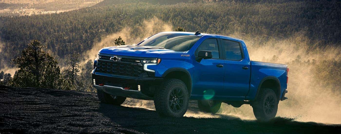 Blue 2025 Chevy Silverado 1500 ZR2 for sale near Rockville driving up a dirt hill.