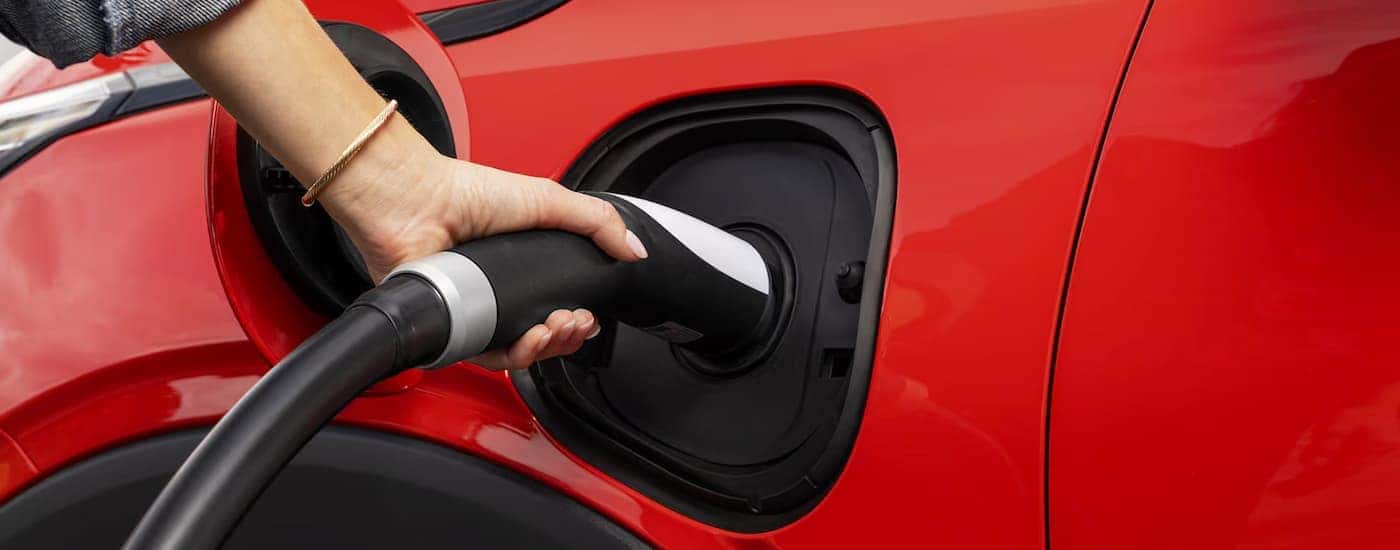 A woman plugging in a red 2027 Chevy Bolt
