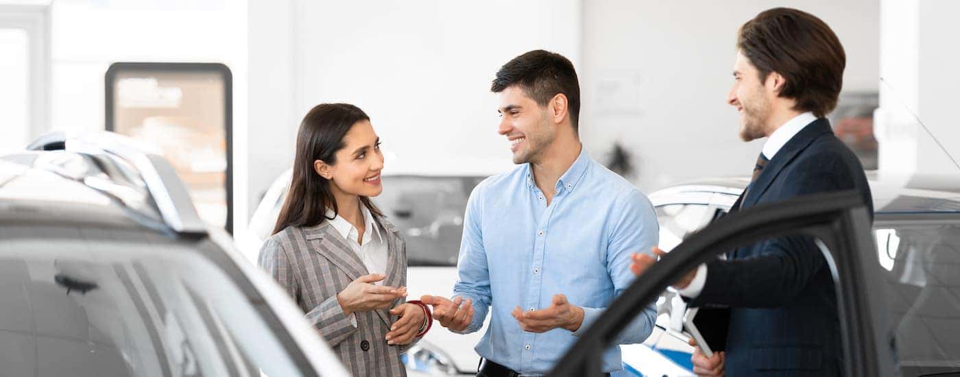 A couple talking to a car salesman at a dealership.