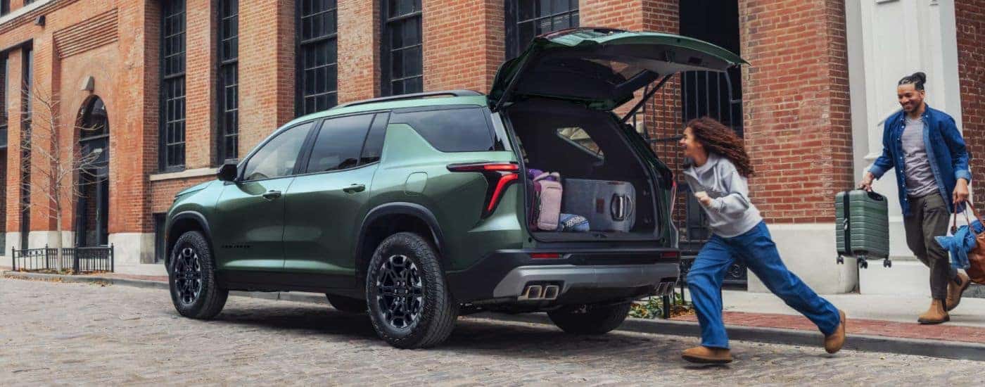 Rear gate open on a green 2027 Chevy Traverse with a family running towards it.