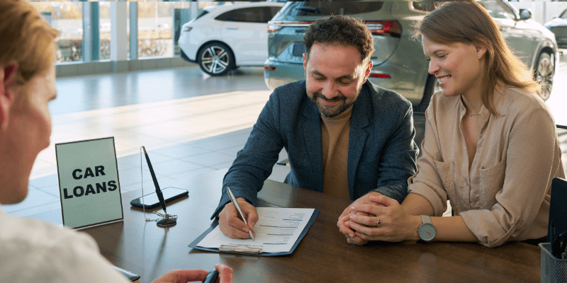 2 adults sitting in car dealership signing up for car loans