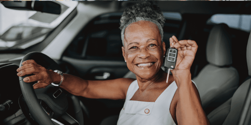 A lady holding up a key inside her new car