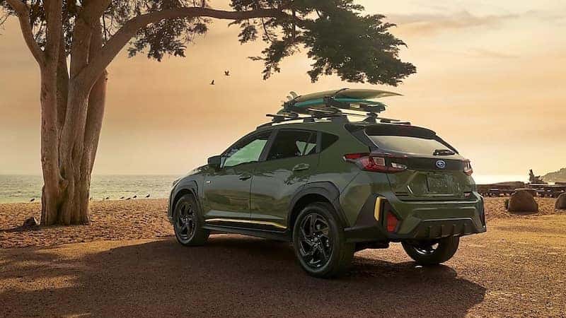 A 2026 alpine green Subaru Crosstrek parked in front of a tree at the beach.