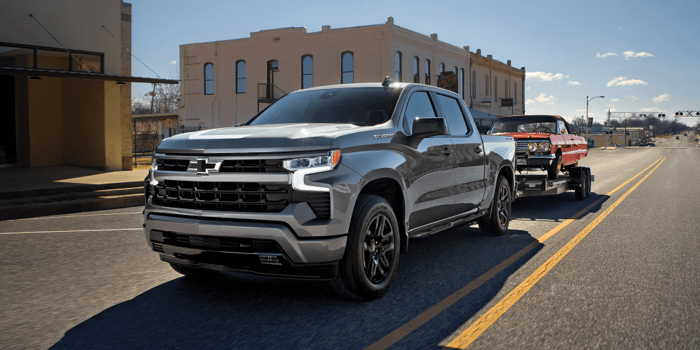 2026 Chevy Silverado 1500 towing classic car on city street