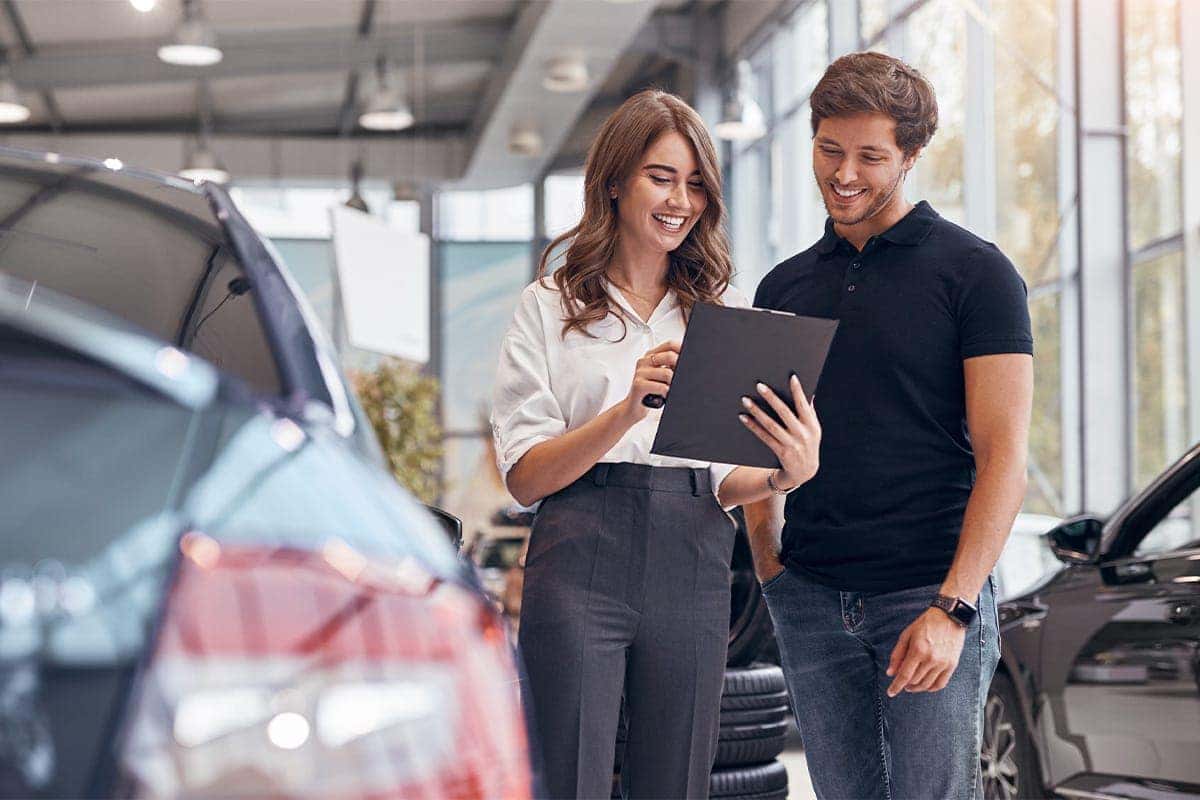 Sales person and customer looking at a tablet next to a vehicle in a dealership