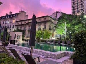An outdoor swimming pool in Buenos Aires during the evening with a purple and pink sky, surrounded by trees and buildings, creating a tranquil urban oasis.
