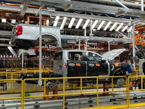 An industrial image of the Ford Ranger plant in Cocheco, Argentina, with vehicles in various stages of assembly on a production line.