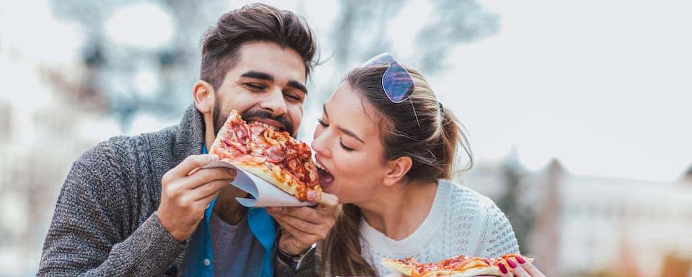 Couple eating pizza outdoors and smiling.They are sharing pizza in an outdoor cafe.